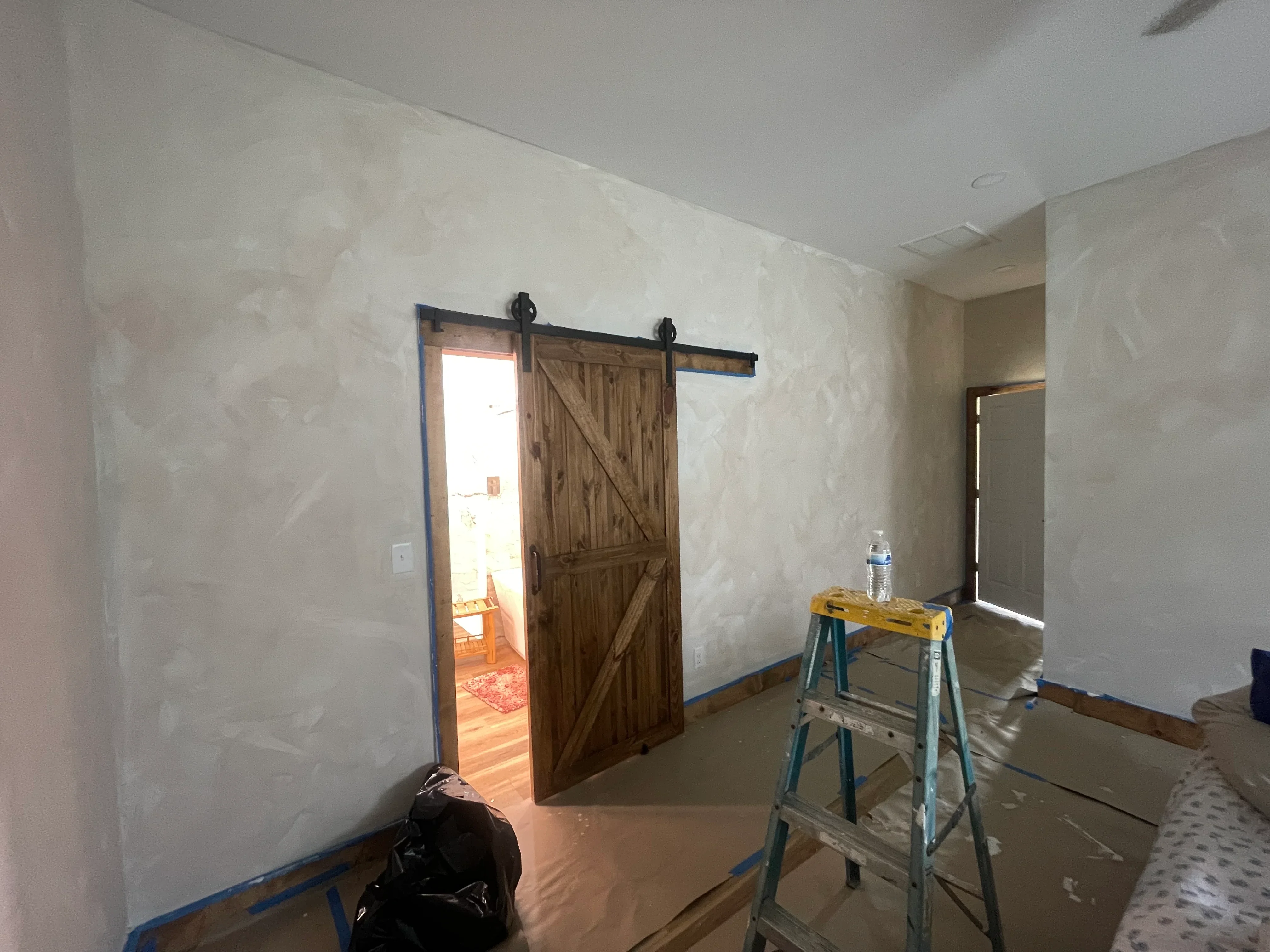 Drywall finishing and rustic barn door with black steel track installation in interior space
