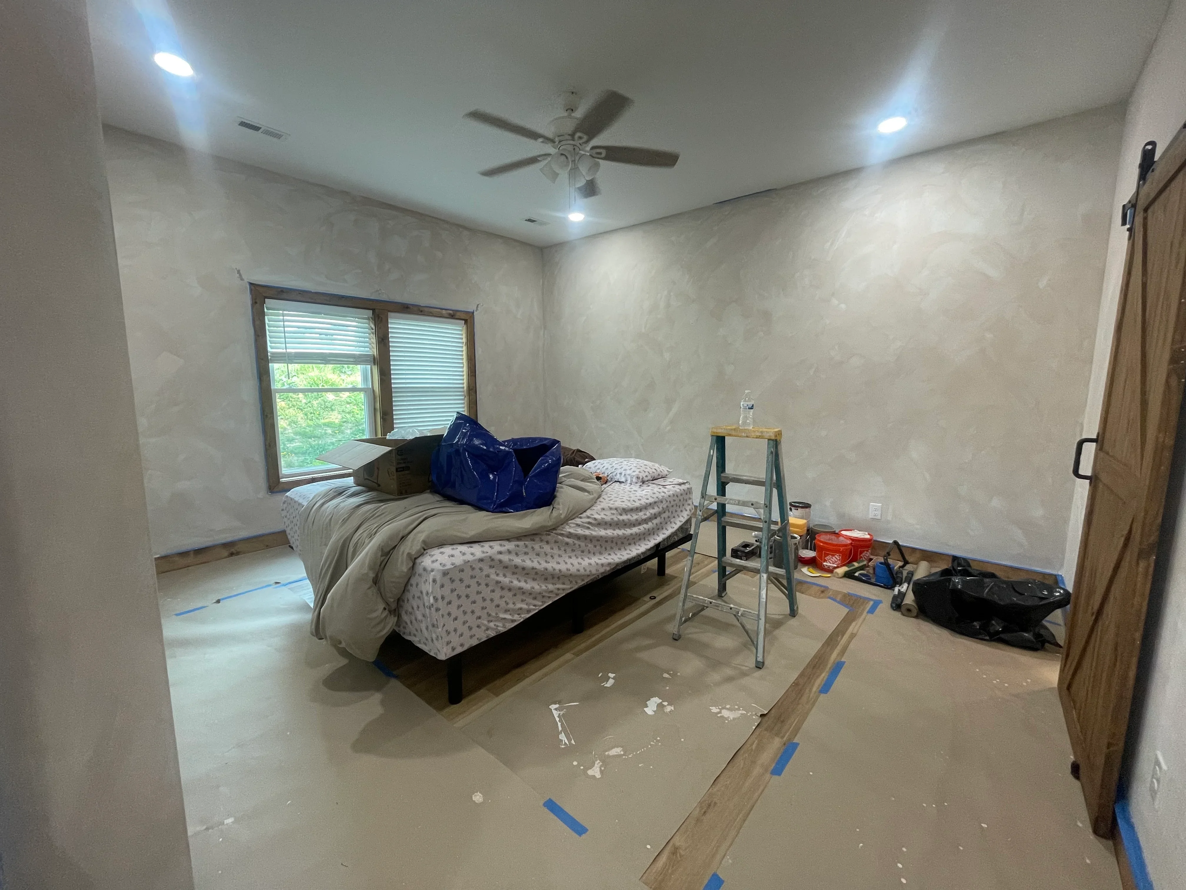 Light gray epoxy floor in bedroom with blue protective tape, recessed lights, and ceiling fan