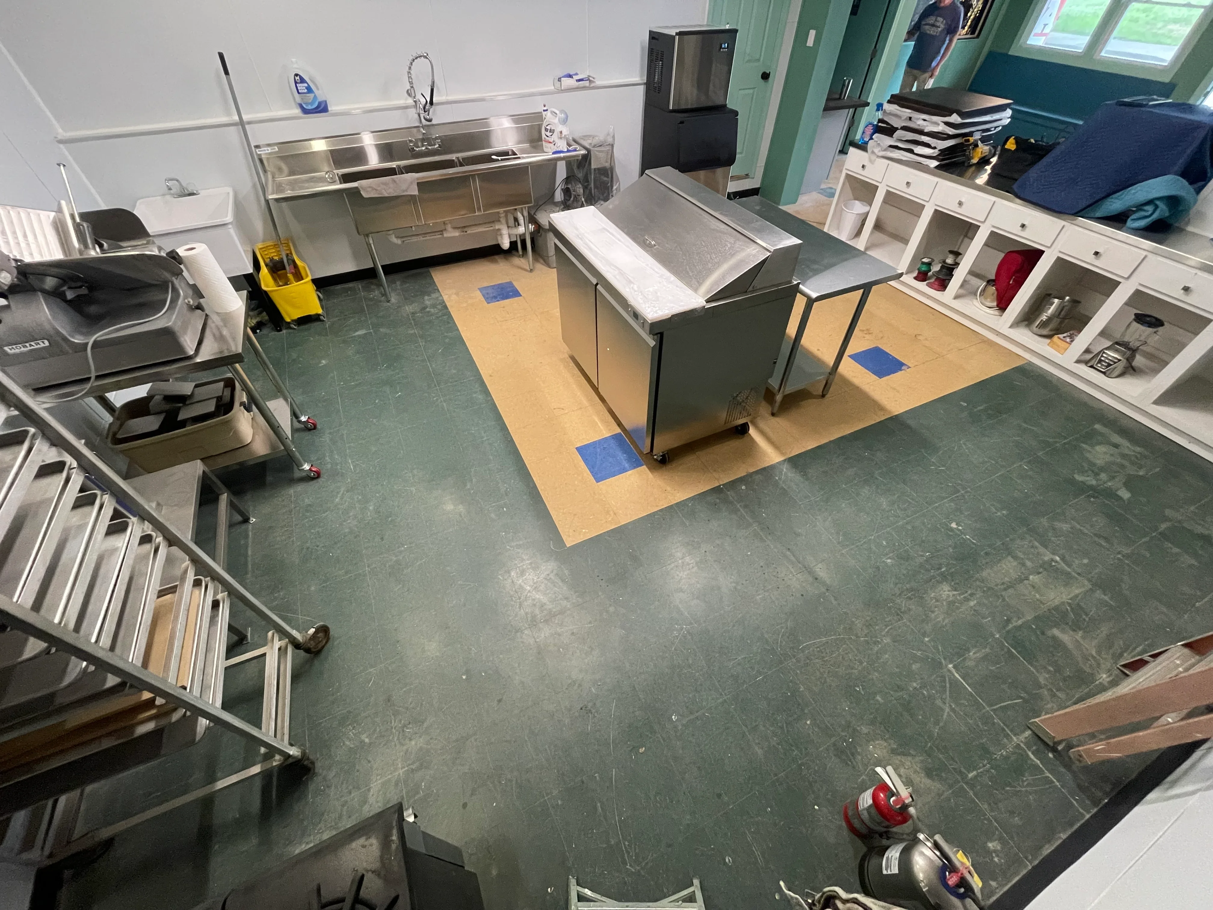 Dark gray epoxy floor with tan accent sections and blue markers in commercial kitchen with stainless steel equipment