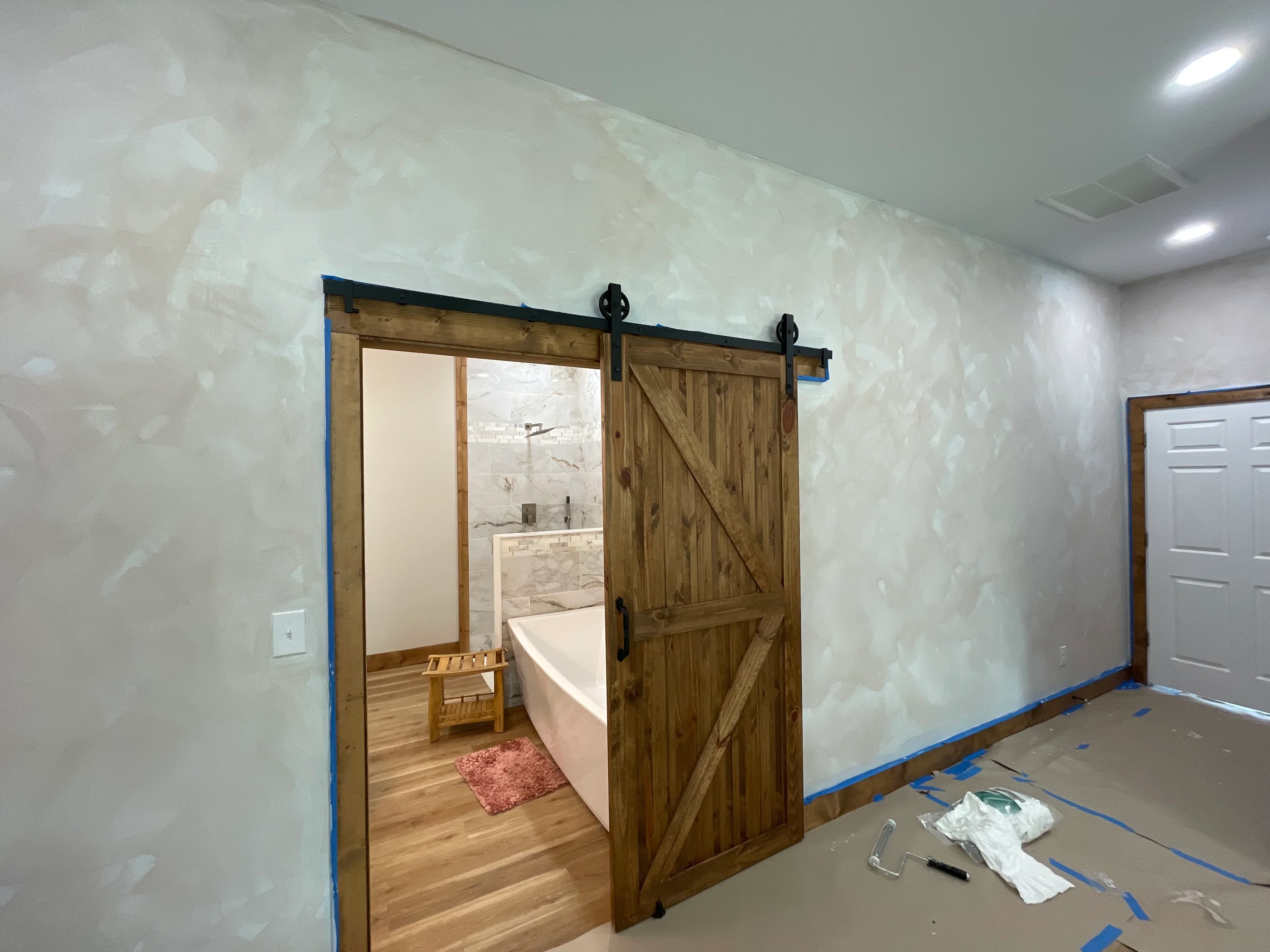 Drywall-finished bathroom with sliding barn door, soaking tub, and marble tile surround