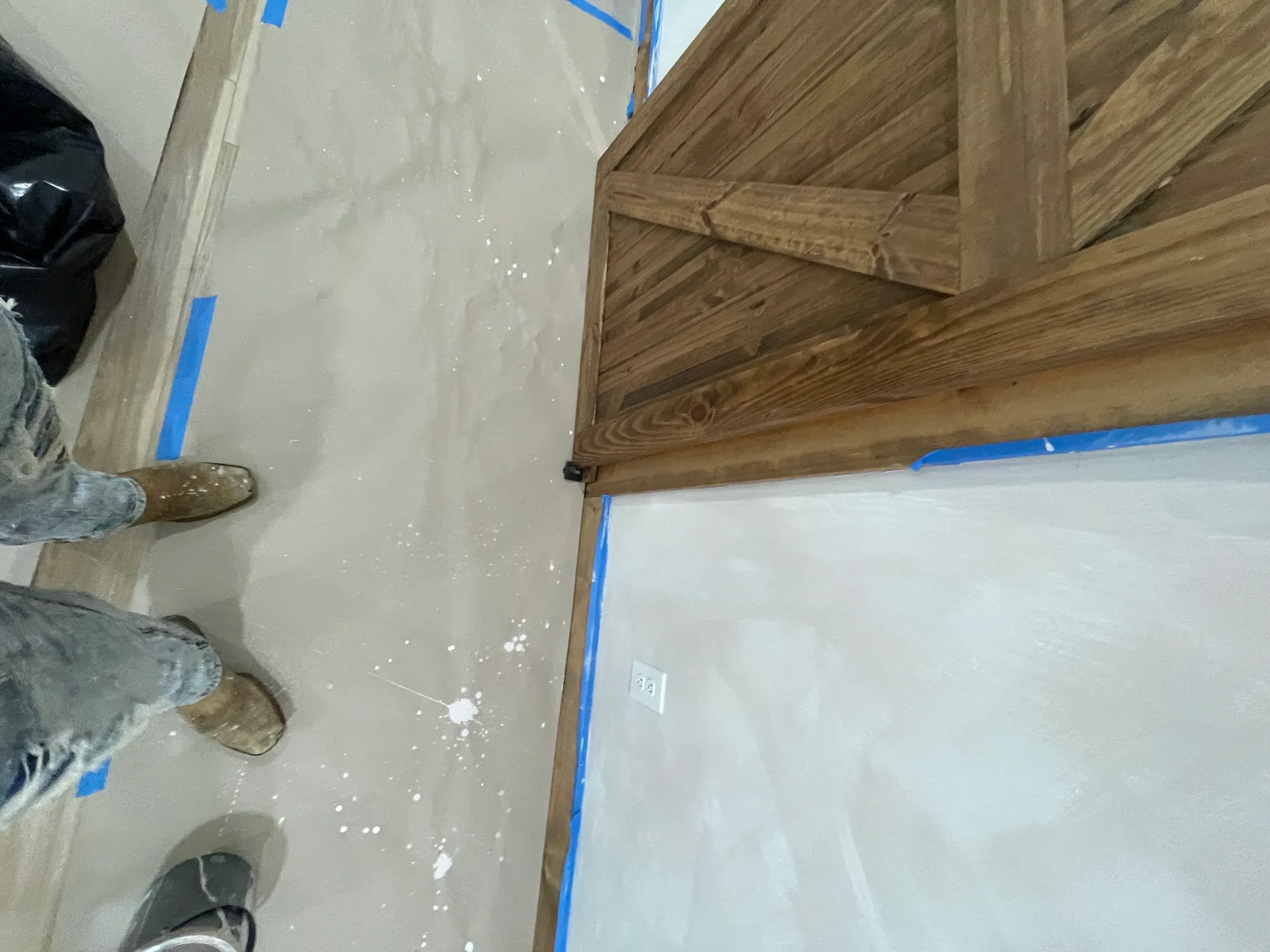 Epoxy floor installation with gray coating and wood baseboard trim, blue masking tape visible