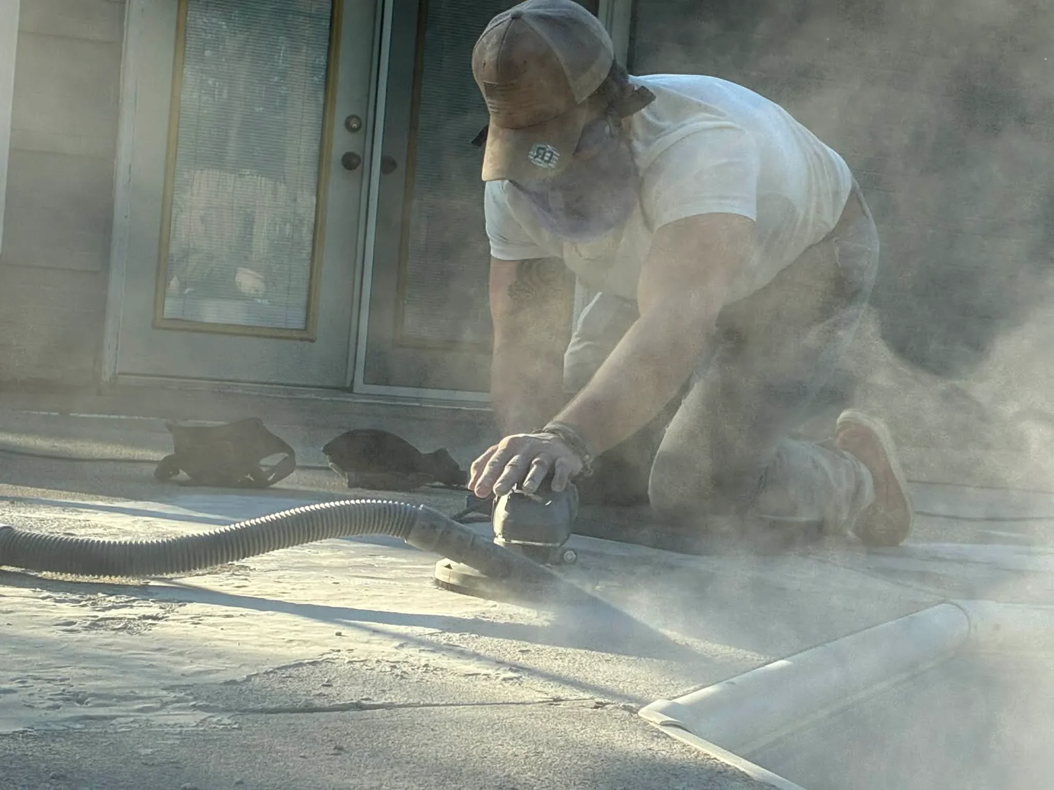 Worker grinding concrete floor with dust collection system near glass door entry