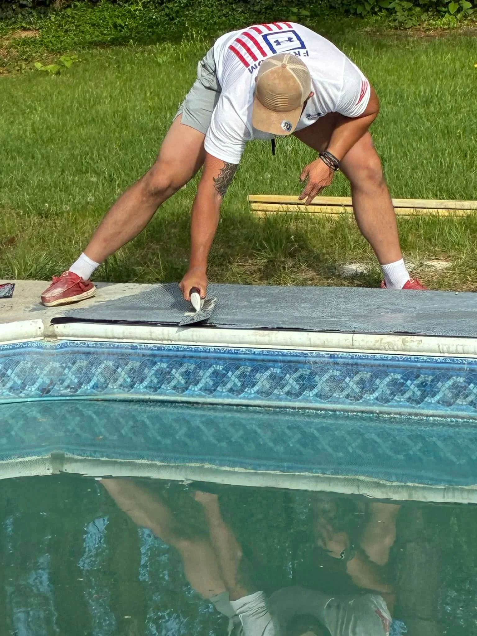 Worker applying epoxy coating to pool deck with decorative tile border pattern