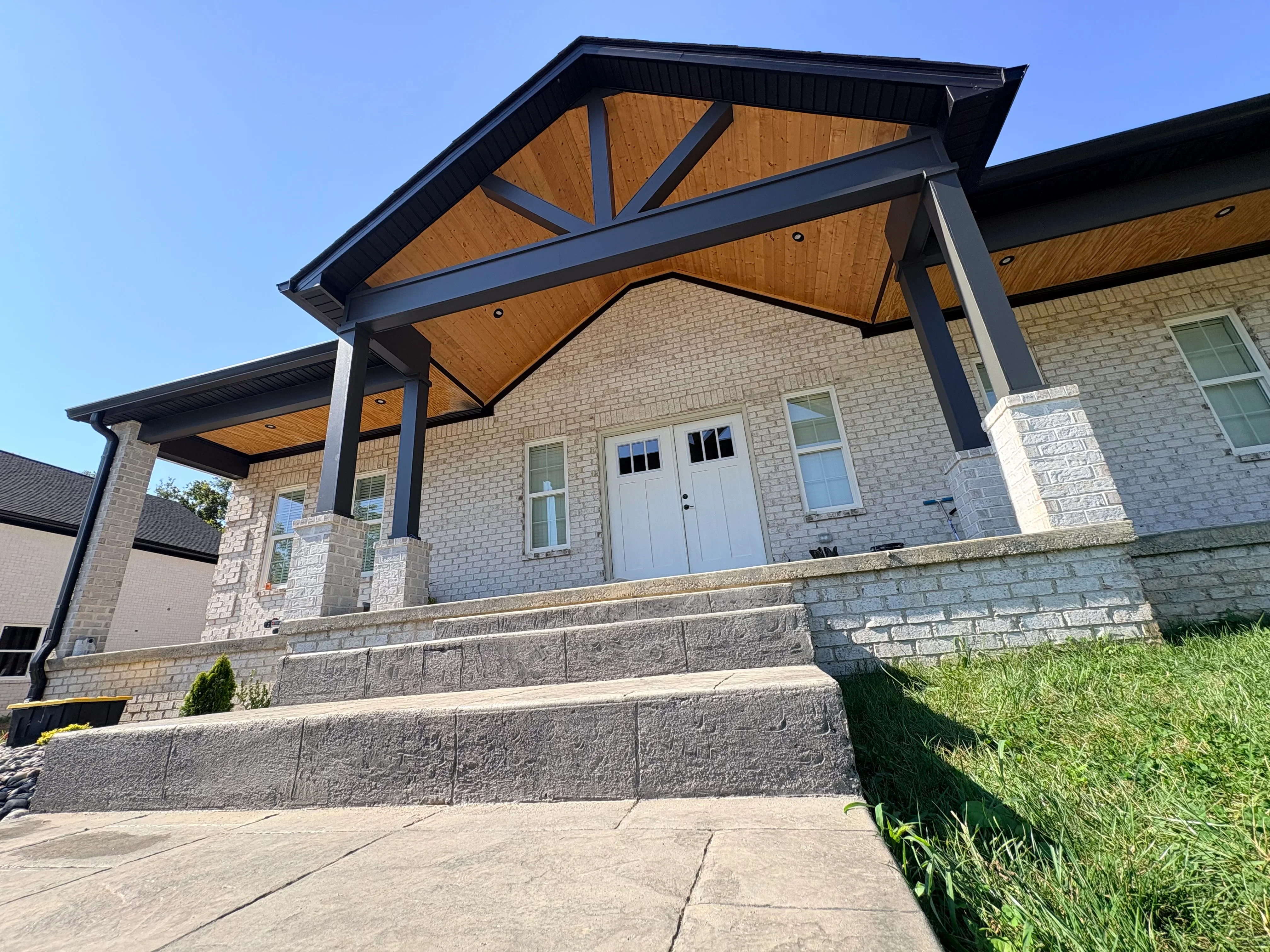 Black steel pergola with wood ceiling panels over brick home entrance